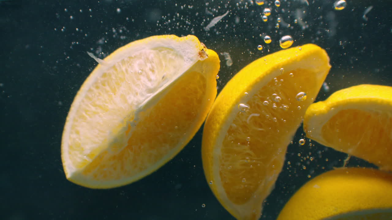 Several lemon fruits fall inside a water tank and disturb water. Three bright yellow lemon fruits fall inside a water tank and return to the surface