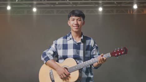 asian teenager with guitar smiling while standing on stage