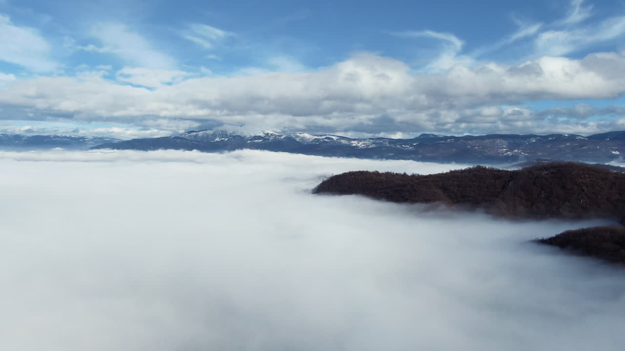 Above the Clouds: Peaks pierce the fog meeting a sky filled with scattered clouds Mountains appear in the distance partially veiled by cloud cover