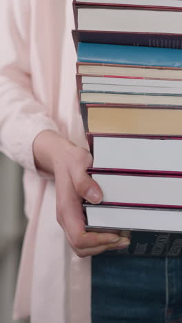 book stack in woman hands closeup. librarian holds high pile of chosen literature walking across library. knowledge base sources for students