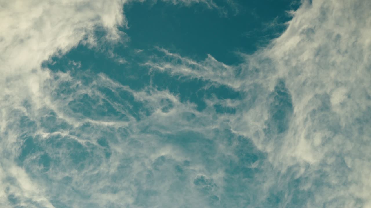 Delicate swirling clouds stretch across a bright blue sky under calm daylight