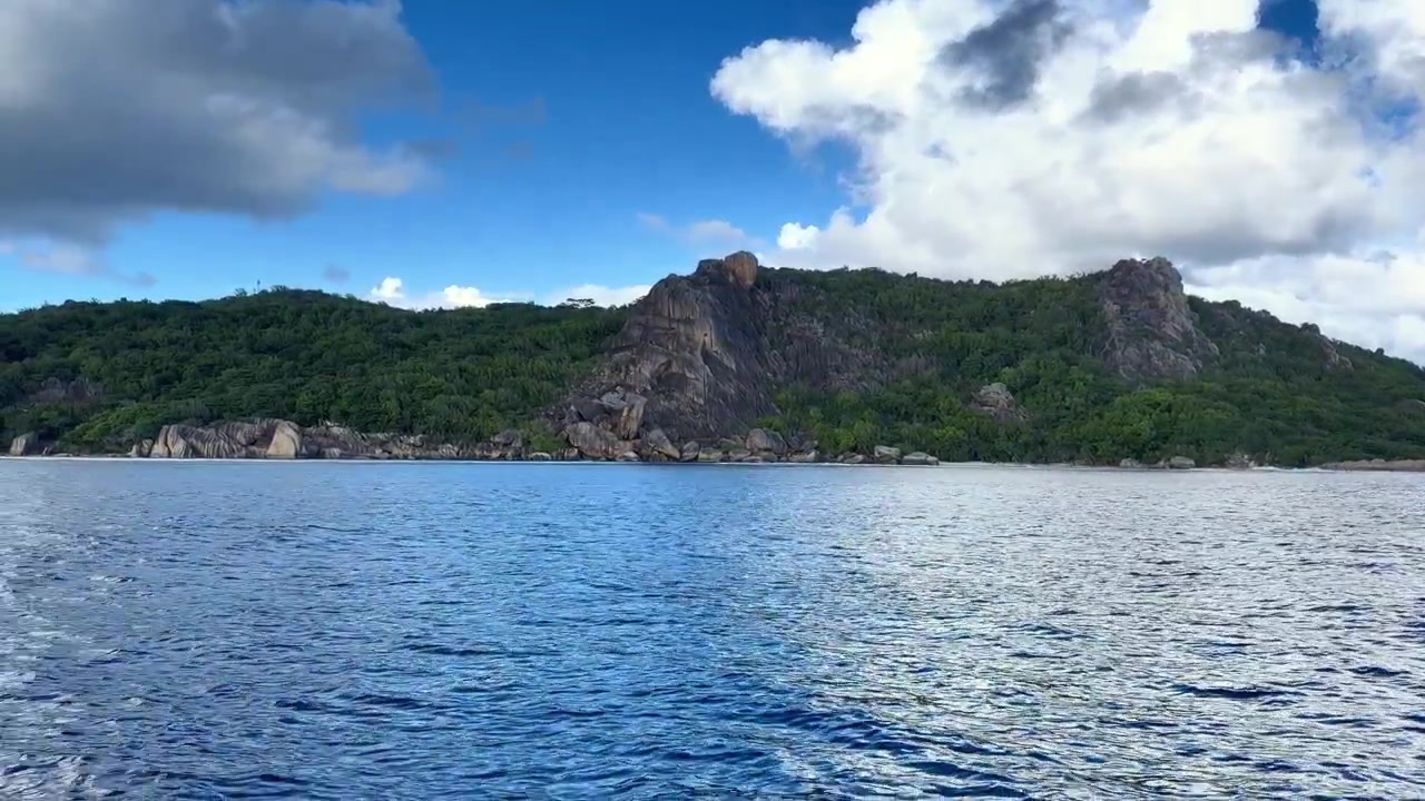 Una bellissima escursione in barca intorno all'isola di La Digue nelle Seychelles, che mostra il profondo blu dell'Oceano Indiano e le drammatiche, lussureggianti colline verdi stratificate con imponenti formazioni rocciose di granito iconiche.