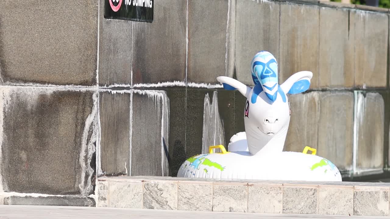 A colorful inflatable unicorn floats near a tiled pool wall with a 'No Jumping' sign.
