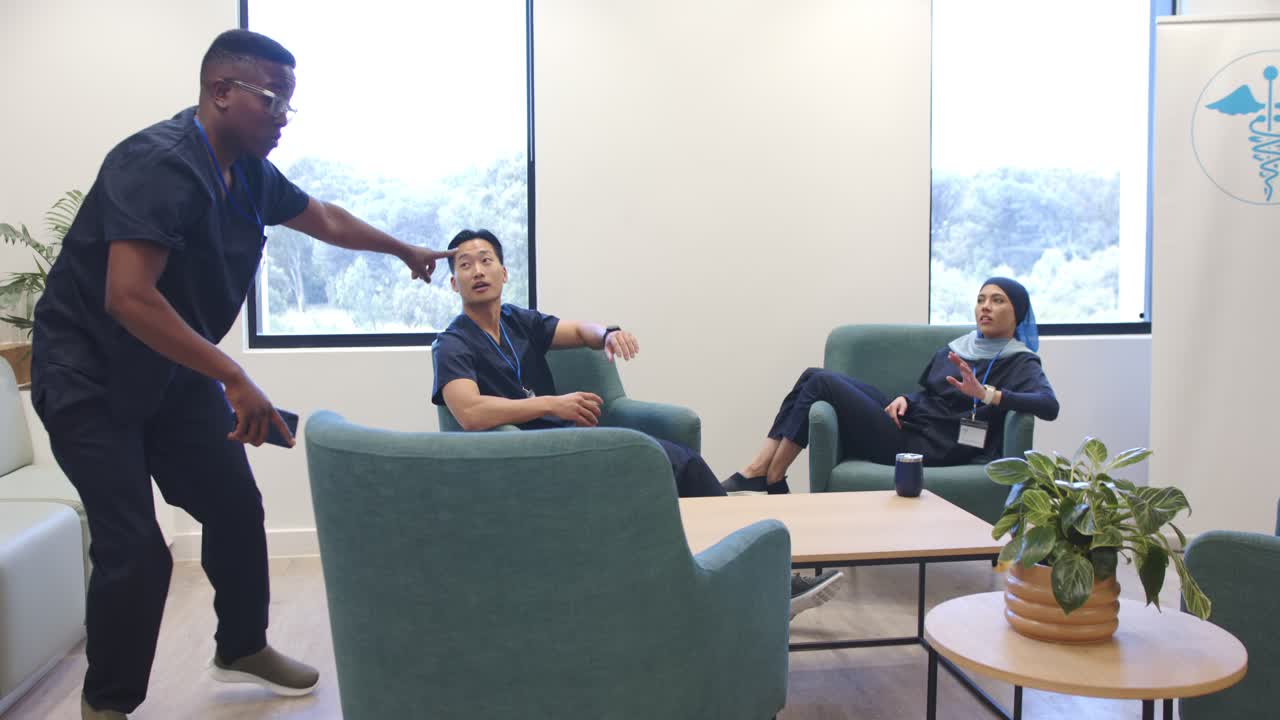 Team di medici in sala relax che reagisce a un avviso mentre un collega si avvicina, si china e indica il telefono
