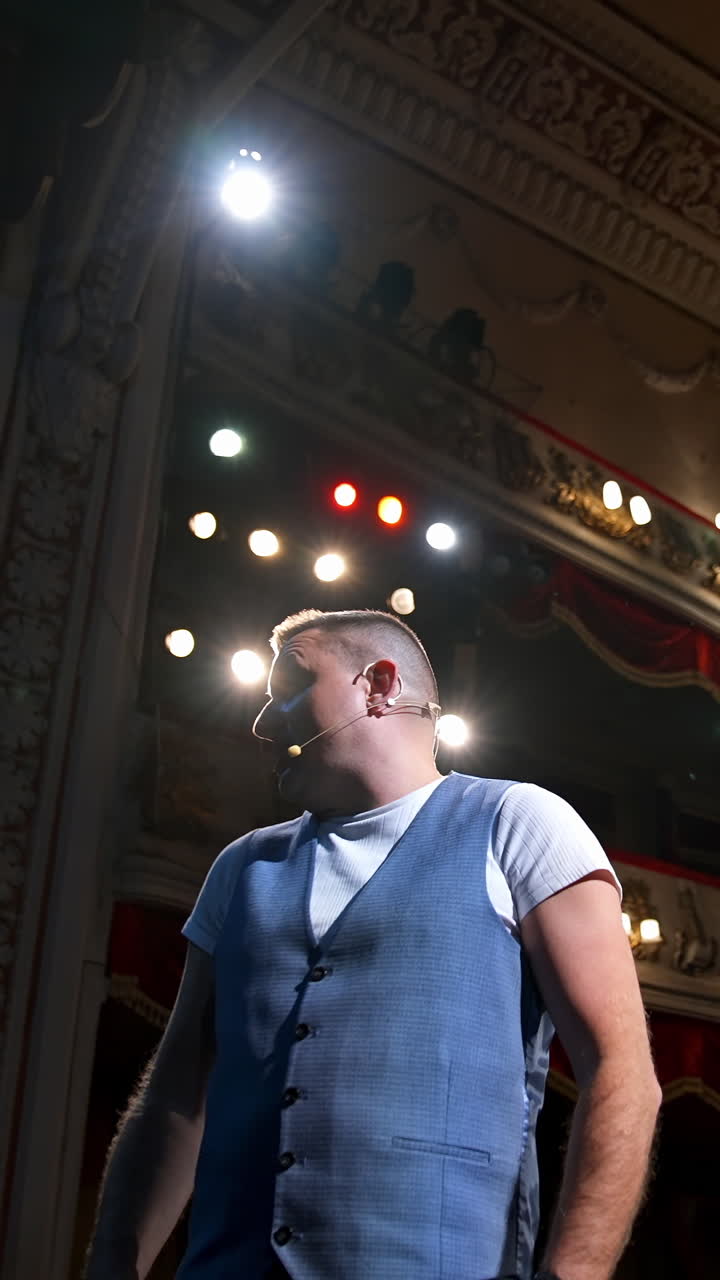 Showman entertains the audience under the light, front view. Big stage. Serious performer speaks from the stage. Hands in pockets. Vertical video