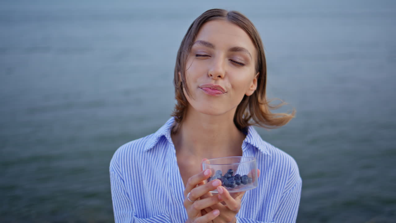 Donna spensierata che gusta dei mirtilli in piedi vicino al mare, primo piano. Donna felice