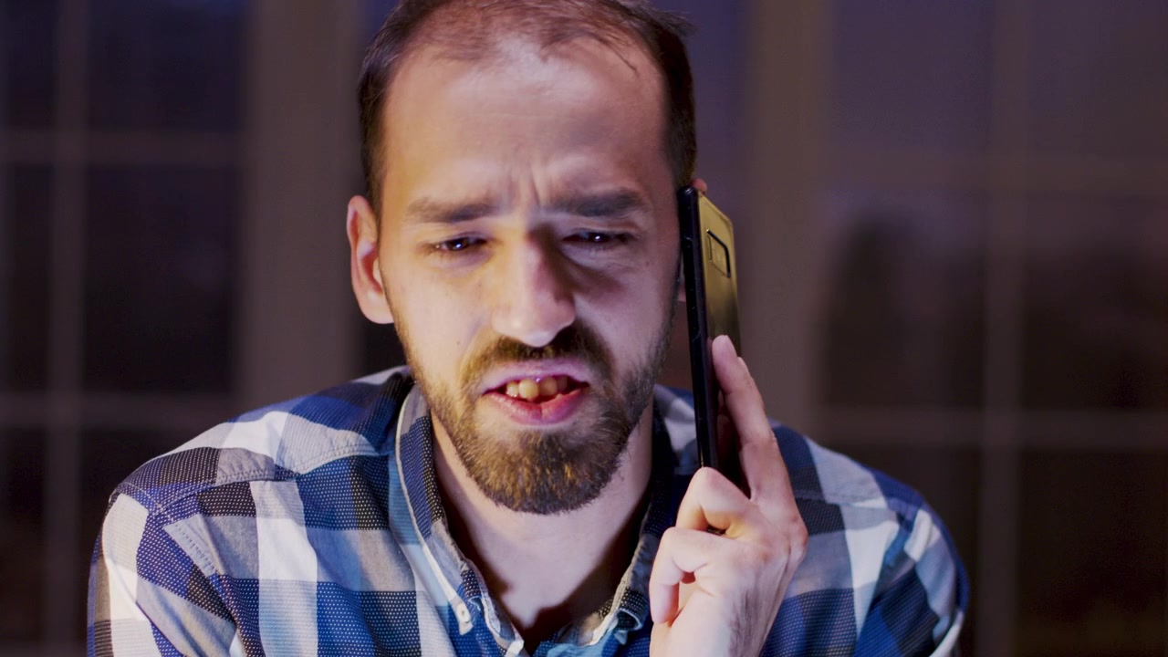 Uomo barbuto che parla allo smartphone mentre lavora fino a tarda notte