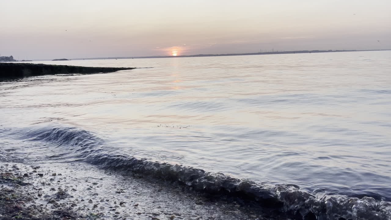 Wide shot showing the sun setting over the sea, showing the waves breaking on the beach