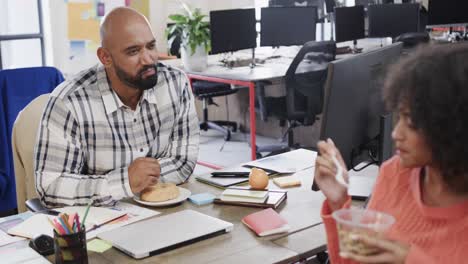 two happy diverse creative colleagues in discussion during lunch in casual office, slow motion