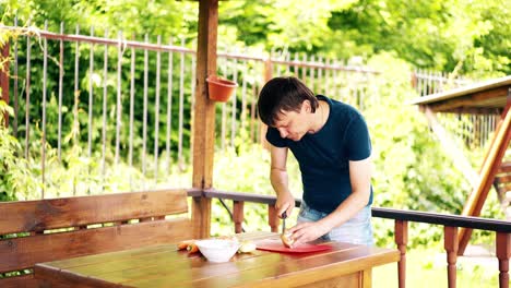 man is standing in a summer house cooking pilaf for a picnic he cleans the onion on a red cutting board