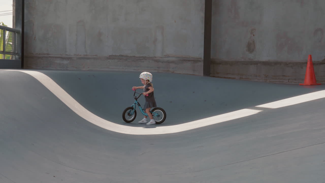 금발 아이가 실내 롤러 스케이팅 경기장에서 자전거를 타고 있다