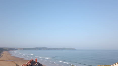 waves crashing against a long sandy beach in devon fading out to blue sky in slow motion