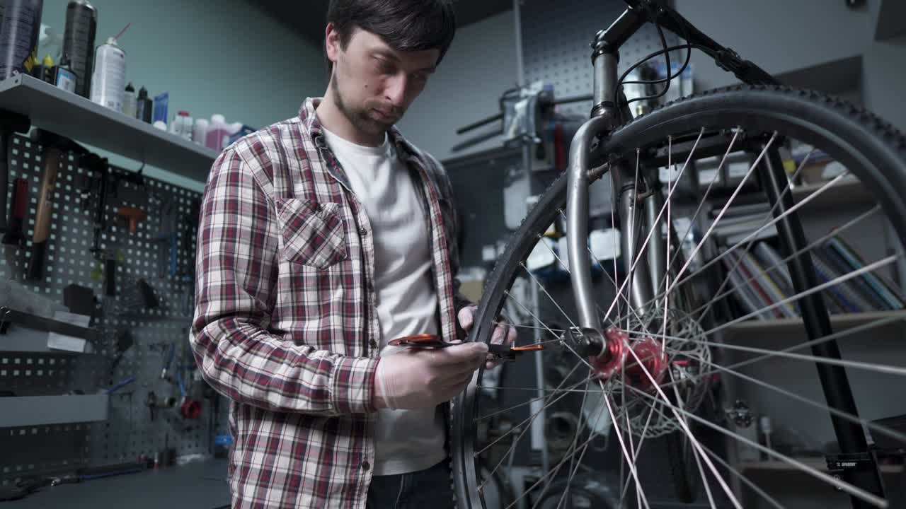 un mecánico de bicicletas masculino alinea los radios de tensión de una rueda de bicicleta con una herramienta especial en el lugar de trabajo en el taller de una tienda de bicicletos. mantenimiento y servicio de la bicicleta. herramienta de alineación del borde de la rueda.