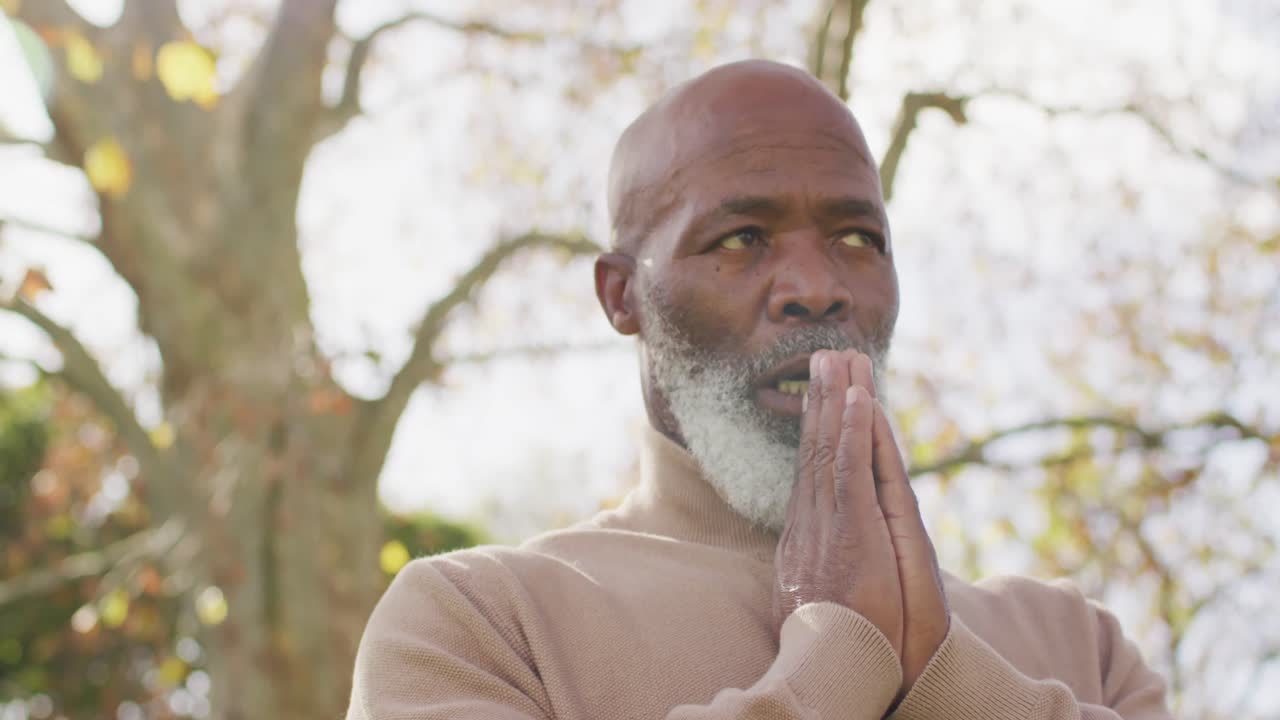 Video of thoughtful senior african american man holding hands in prayer in garden