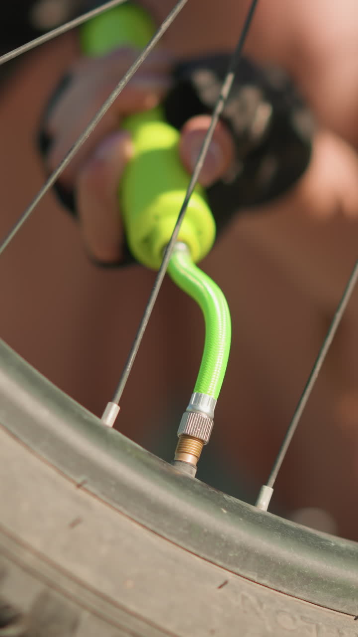 primer plano de un neumático de bicicleta inflado con una bomba de aire, destacando la válvula del neumático y la boquilla de la bomba verde, persona ligeramente borrosa en el fondo, centrándose en el mantenimiento de la bicicleta