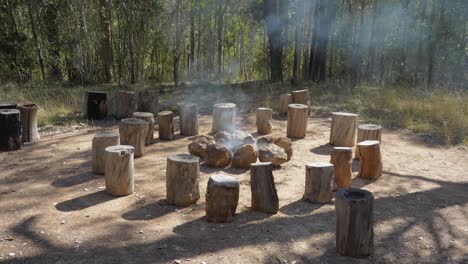 Baumstümpfe-Rund-Um-Die-Feuerstelle-Mit-Rauch,-Der-Aus-Den-Brennenden-Baumstämmen-Aufsteigt---Campingplatz-In-Mount-Byron,-Queensland,-Australien