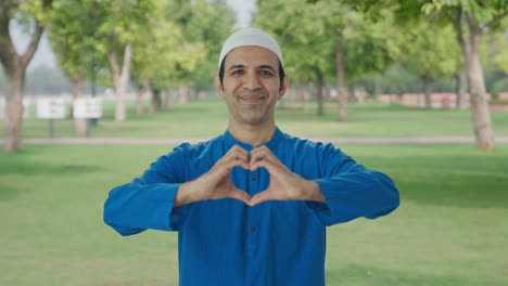 happy muslim man smiling and showing heart sign in park