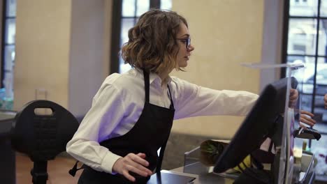 smiling female cashier in black apron and unrecognizable customer paying with her ec card at supermarket checkout and taking her