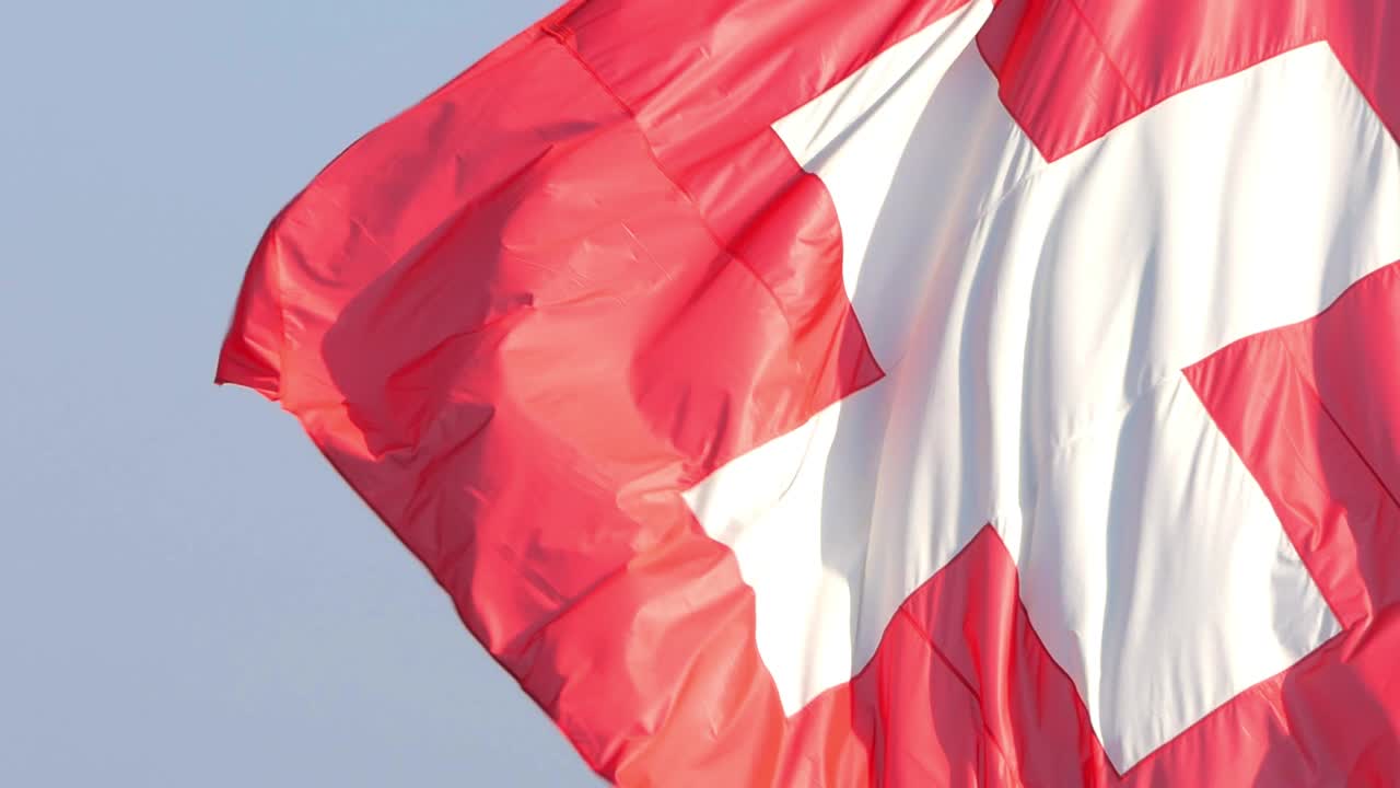 Zeitlupen-Nahaufnahme einer Schweizer Flagge, die an einem sonnigen Tag im Wind weht.