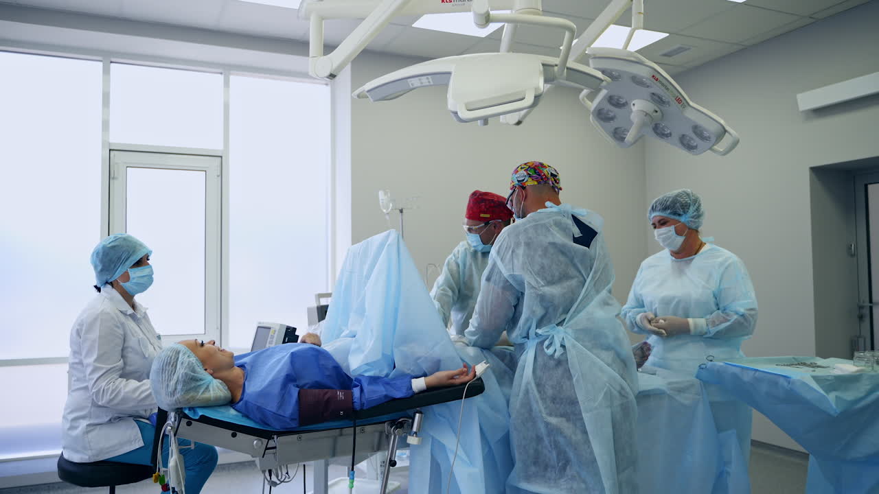 Surgical team performing vascular operation in modern surgical room. Conscious female patient talks to the doctors operating her.