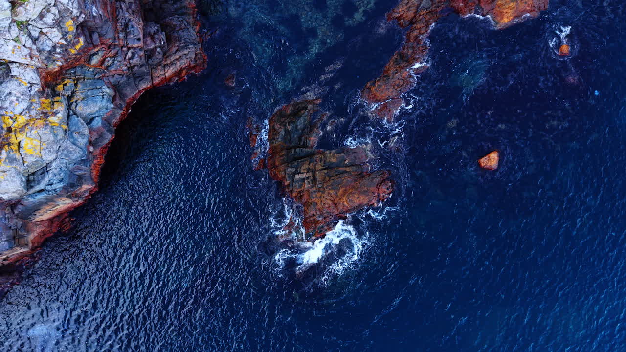 Isolated rock formation in clear sea. Lone jagged structure sits surrounded by vivid deep water in an overhead view