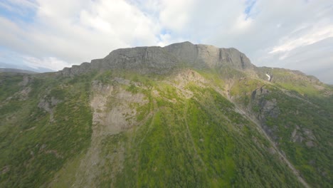 Ascend-flight-to-mountain-top-rossnos-with-green-forest-in-Norway-during-sunlight