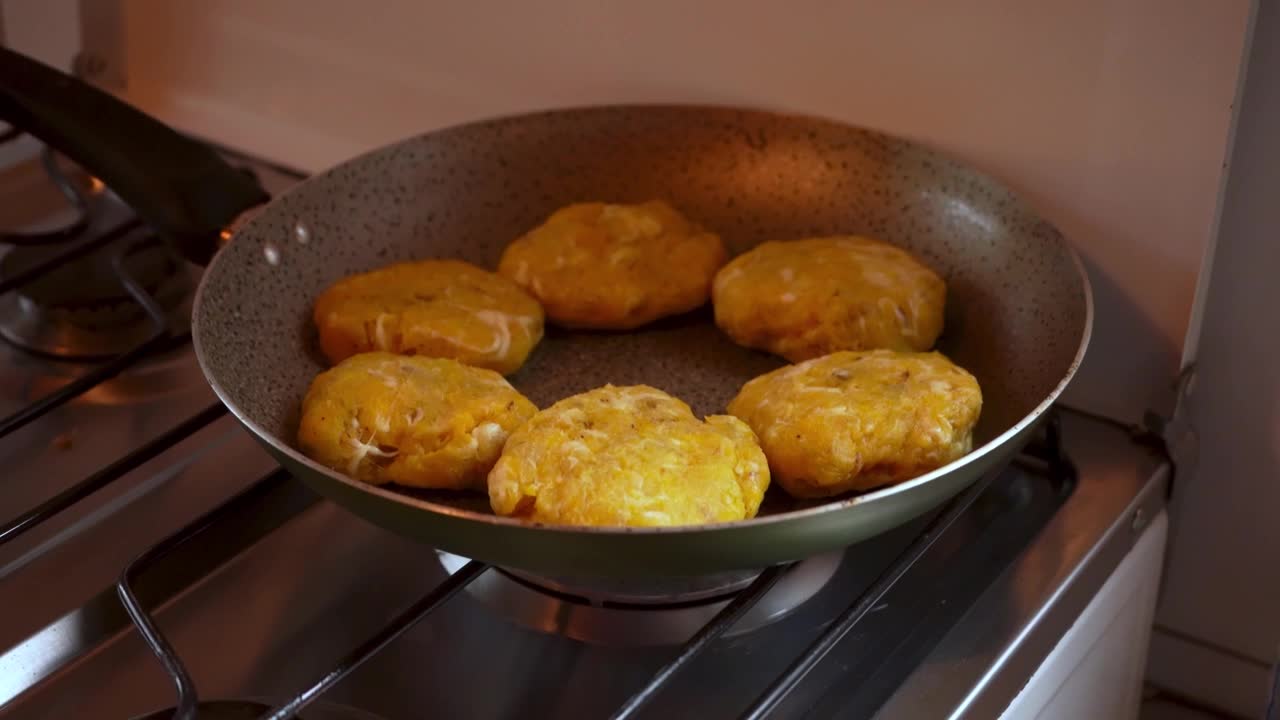Dolly out of ripe plantain and cheese patties frying in a nonstick pan over gas stove. Latin American homemade cooking. Great for recipes or food content.