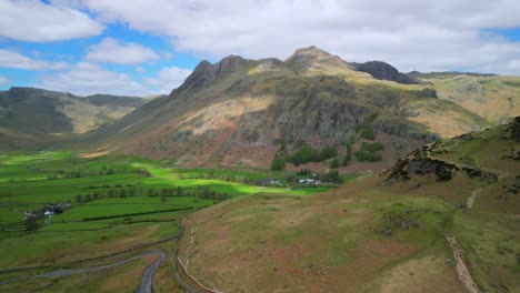 Mountain-shoulder-flypast-towards-Langdale-Pikes-mountain-range-with-reveal-of-sun-speckled-wider-green-valley-floor