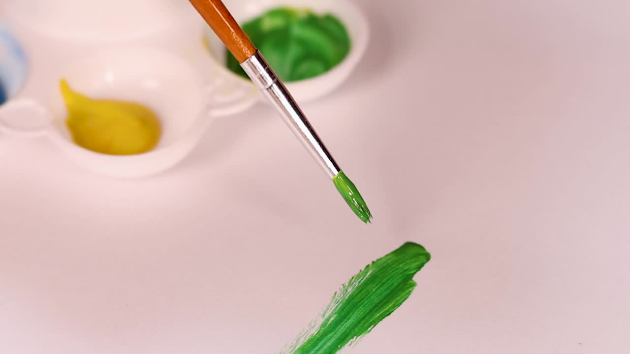 Un pennello applica una vivace pennellata verde ad acquerello su carta bianca accanto a una palette
