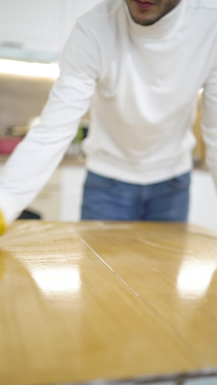 Vertical video shows a man polishing a table with a microfiber cloth, emphasizing gentle cleaning, dust removal, and household maintenance during spring cleaning at home