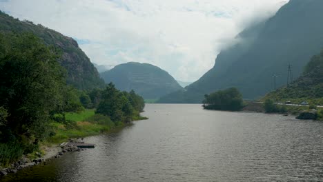 the river winds gently through lush greenery, embraced by towering mountains. soft clouds hover above, casting shadows on the water's surface, creating a peaceful atmosphere