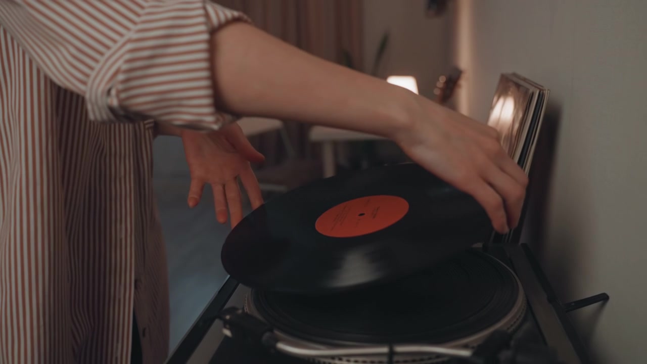 Postazione di registrazione con cuffie pronte. Primo piano delle mani che posizionano con cura il disco sul giradischi che gira. Scena dettagliata che mostra la manipolazione precisa del vinile e delle cuffie prima che la musica inizi.