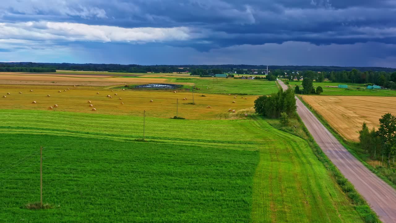 Straight road cutting through farmlands under brooding sky with hay fields in aerial view