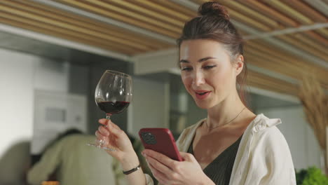 woman browsing phone and drinking red wine at home