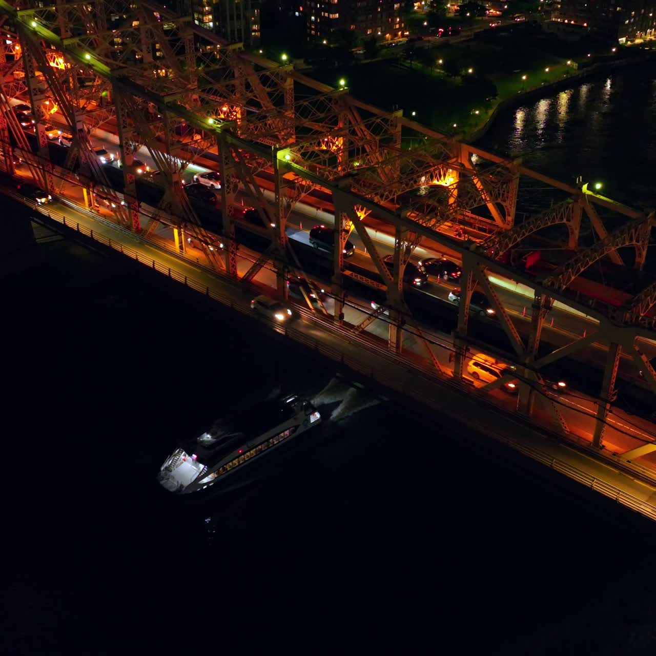 Traffic jams on the big bridge at night time. Launch going under the bridge along dark river. Top view