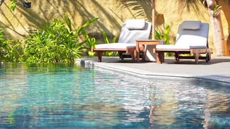 two empty sun loungers face a resort swimming pool