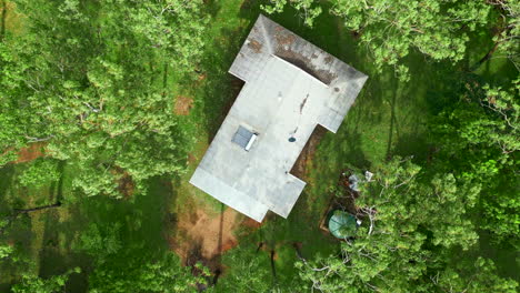 Aerial-drone-of-Rural-Estate-Acerage-With-Dirty-Corrugated-Roof-and-Moss,-Ascend-Top-Down-Spin-past-Trees