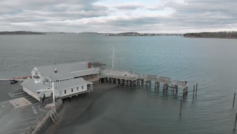 Hingham-Yacht-Club-At-Hingham-Harbor-In-Massachusetts-With-Distant-View-Of-Boston-Harbor-On-A-Cloudy-Day---aerial-drone