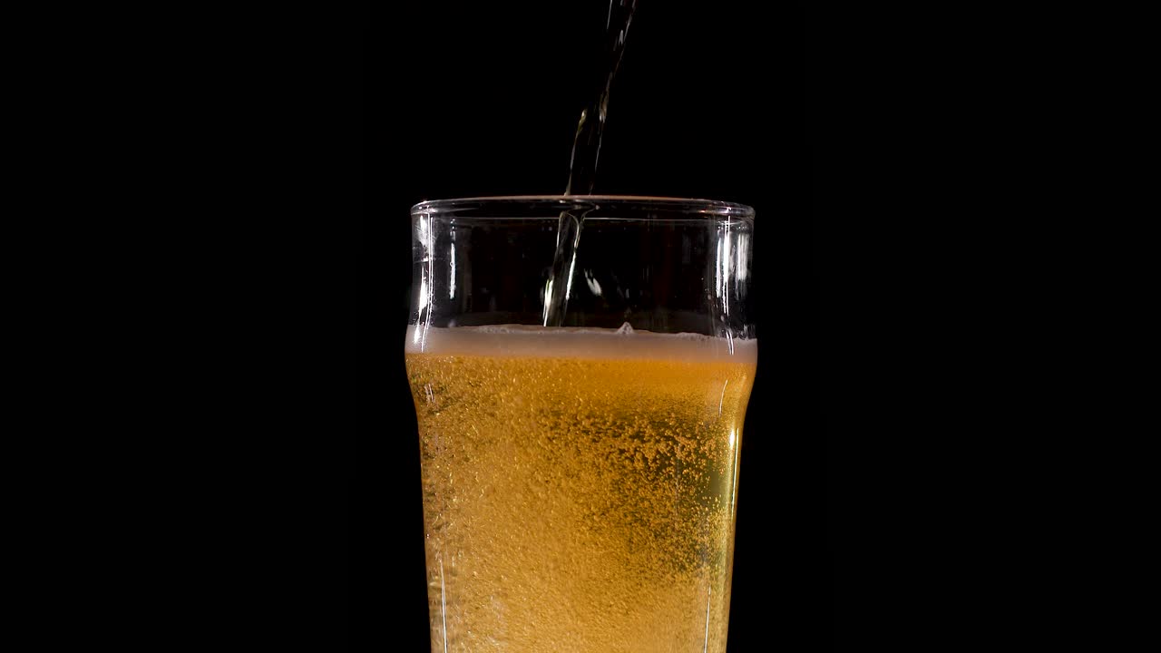 Birra versata al rallentatore in un bicchiere su uno sfondo nero infinito
