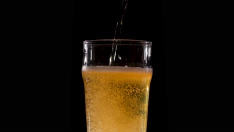 cerveza en cámara lenta vertiendo en un vaso sobre un fondo negro sin fin
