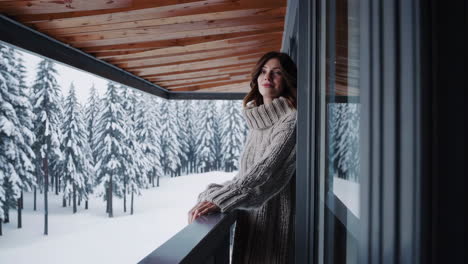 woman in cozy sweater enjoying a snowy winter forest view from a balcony