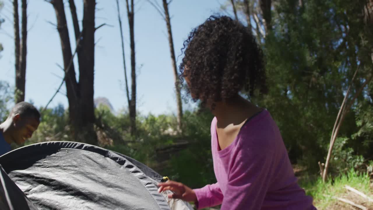 Coppia multietnica sorridente che monta la tenda all'accampamento in campagna.