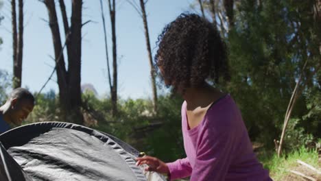 Smiling-diverse-couple-preparing-tent-at-camp-in-countryside