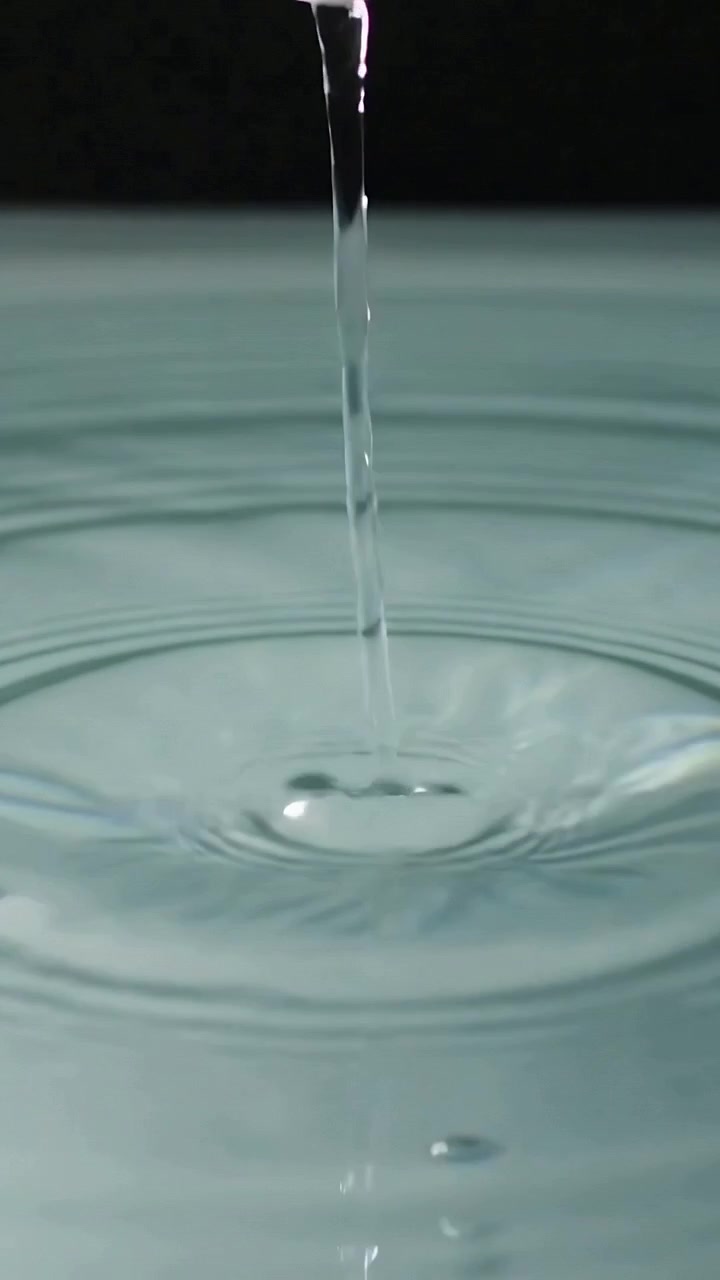 Vertikal video: Frigiver tynd vandsøjle, hvid dyse sender ringe hen over lav turkis pool
