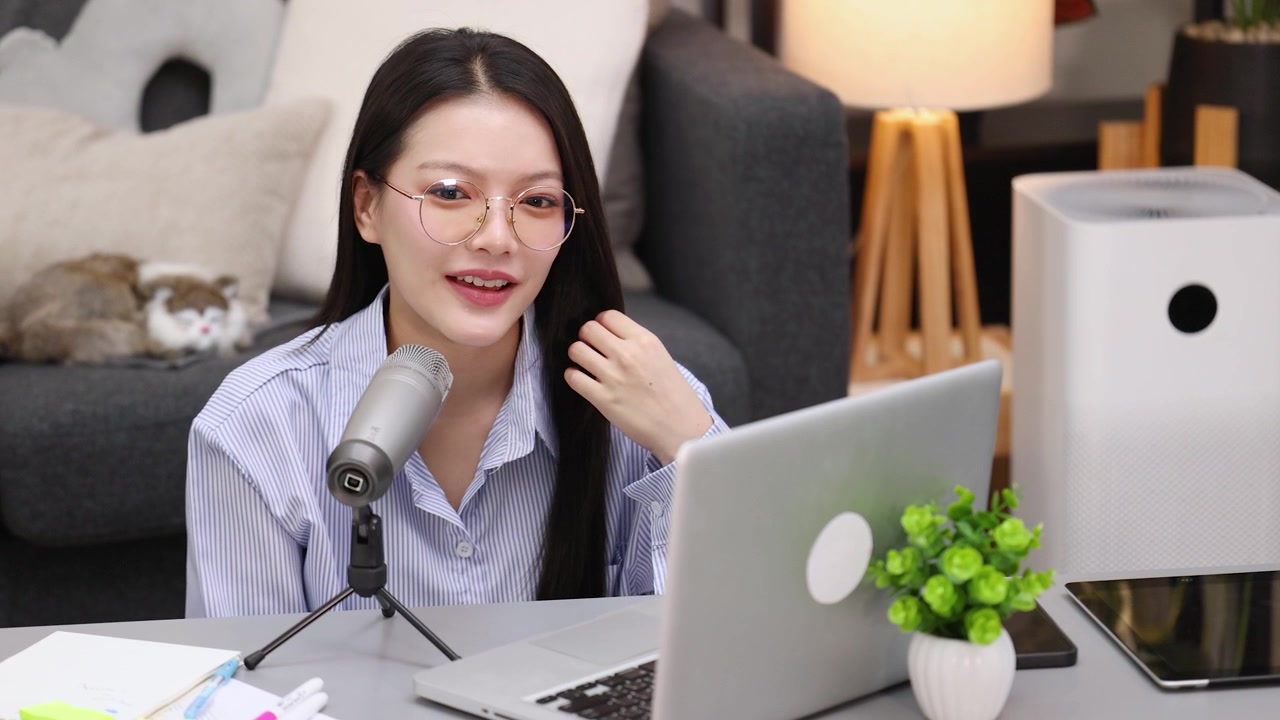 自宅からのビデオ通話中にマイクに向かって話す、眼鏡をかけたアジア人女性