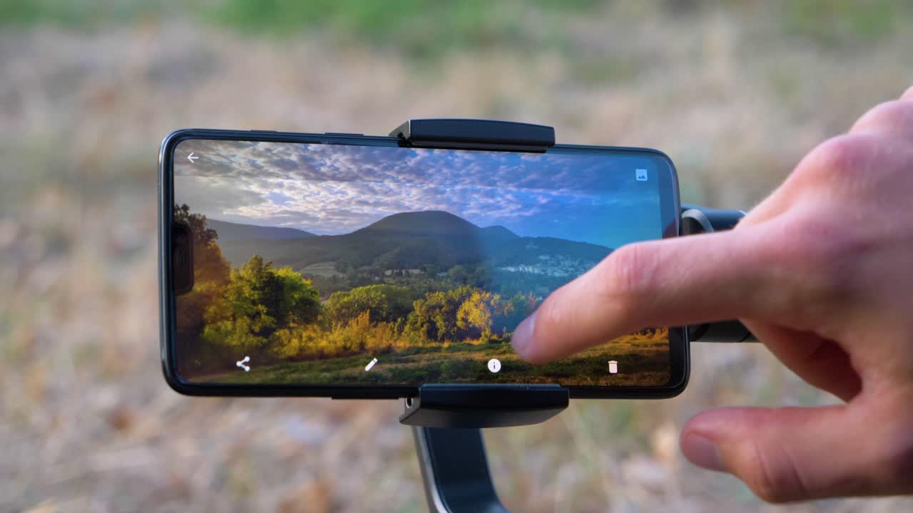 hombre retocando una imagen de paisaje en su teléfono inteligente en un gimbal en cámara lenta smartphone de muesca sin marca