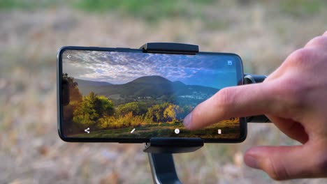 Mann-Retuschiert-Ein-Landschaftsbild-Auf-Seinem-Smartphone-Auf-Einem-Gimbal-In-Zeitlupe,-Notch-Smartphone-Ohne-Marke