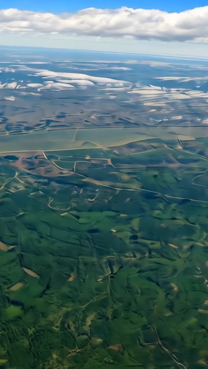 Vertical video: Tilting aerial view over farmland showing hedgerows, roads, river, hills, clouds