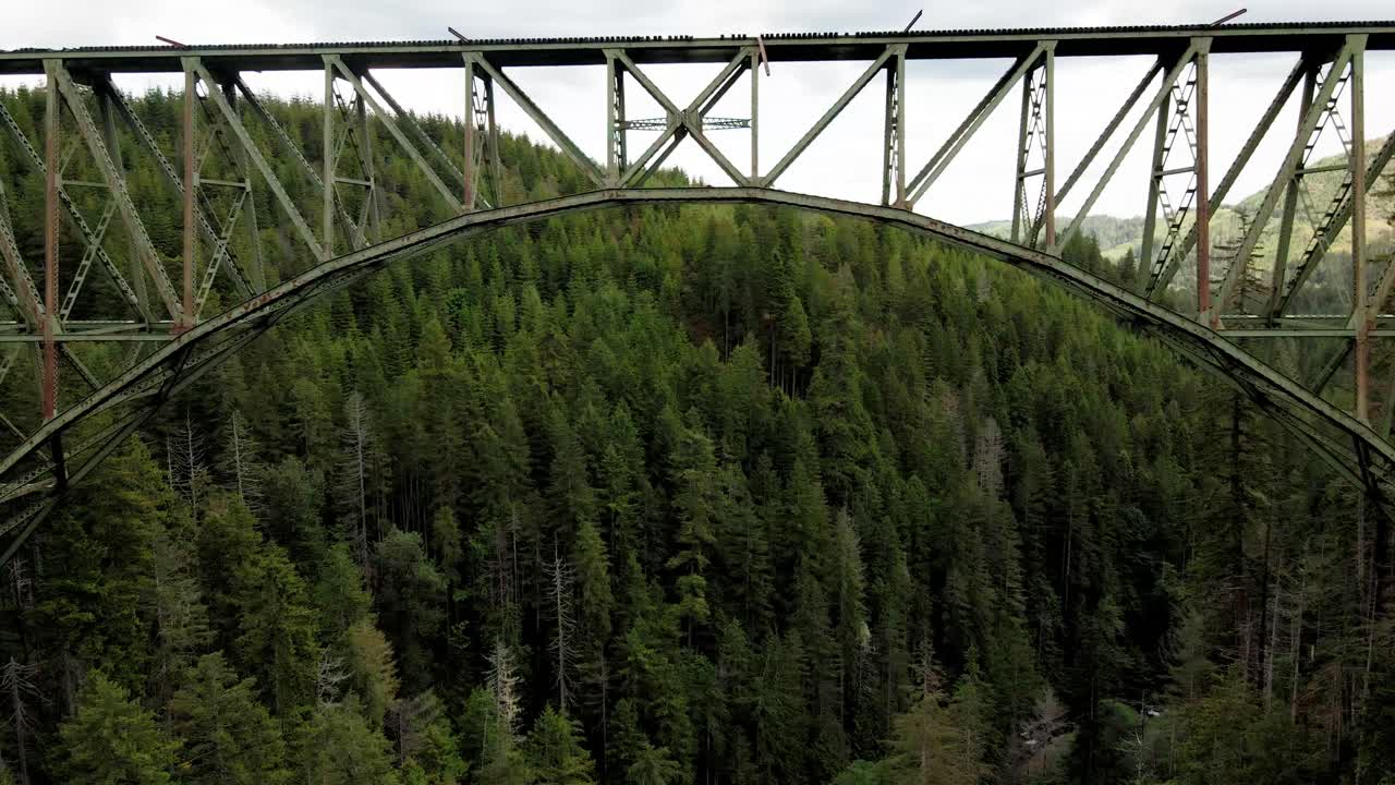 volando debajo de un puente y encima de un bosque, el puente de acero alto es un puente de arco de armadura que se extiende por la bifurcación sur del río skokomish en el condado de mason, washington