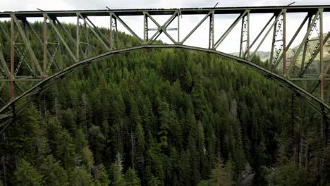 flying below of a bridge and on top of a forest, The High Steel Bridge is a truss arch bridge that spans the south fork of the Skokomish River in Mason County, Washington